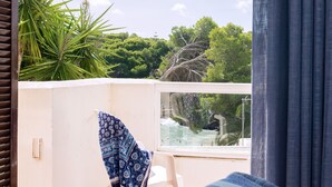 Ein Balkon mit Blick auf ein Schwimmbecken und Bäume, ein weißer Stuhl und eine gemusterte Decke.