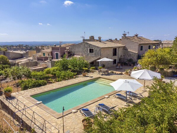 A pool area with lounge chairs and umbrellas, surrounded by stone buildings and greenery. - Sa Rota by Interhome (Biniamar)