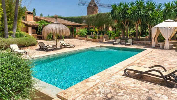 Une piscine avec des chaises longues, un moulin à vent et une structure à toit de chaume.