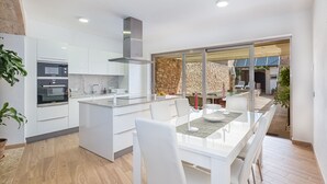 Une cuisine moderne avec des meubles blancs, un four encastré et un coin repas comprenant une table à plateau en verre et des chaises blanches.