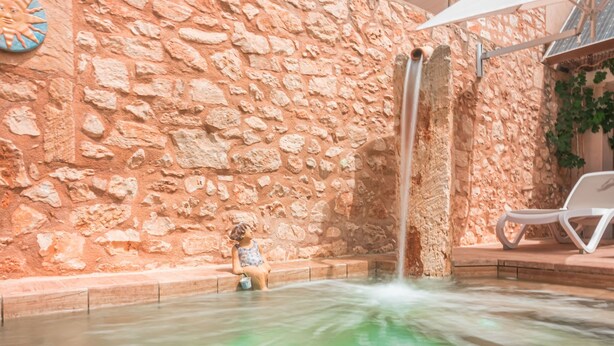 Un mur de pierre agrémenté d’un élément décoratif aquatique, une sculpture représentant un enfant et un fauteuil de relaxation.