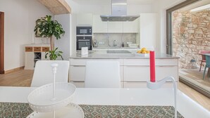 Une cuisine moderne avec des armoires blanches, une hotte de cuisinière en acier inoxydable et un mur en pierre adjacent à la cuisine.