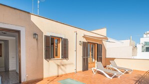 Una terraza en la azotea con dos tumbonas, una puerta pequeña y una ventana con persianas.