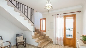 Una escalera con detalles de madera, un candelabro, una puerta de madera con vistas y una silla con cojín.