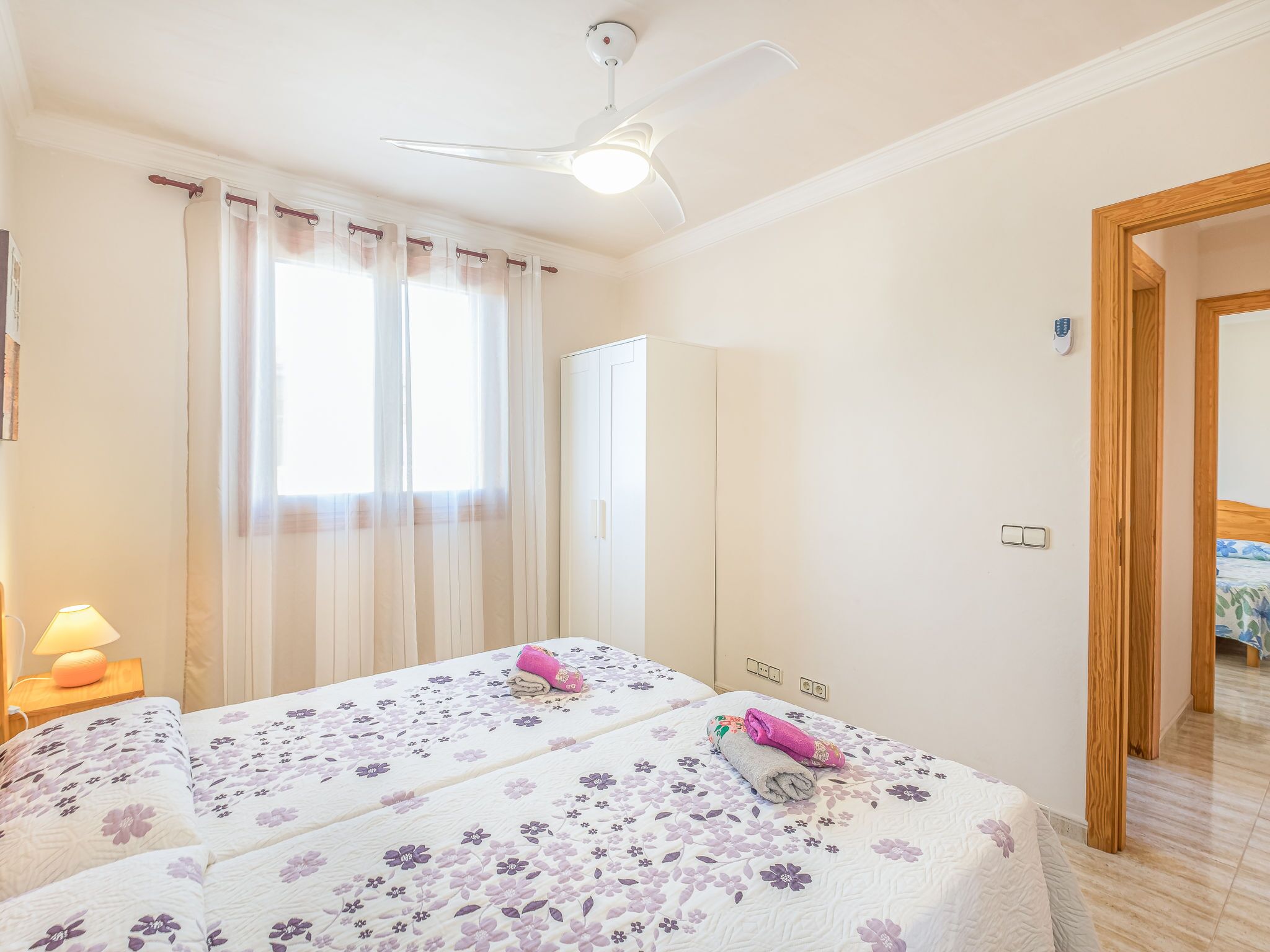 Ein Hotelzimmer mit zwei Betten, einem Deckenventilator, einem Fenster mit Vorhängen, einer Nachttischlampe und einer Holztür.