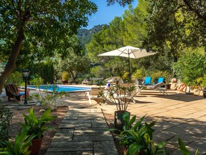 Zona de piscina con cubierta de madera, sillas de descanso y una sombrilla grande.