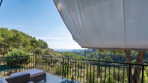 Ein Balkon mit Korbmöbeln, einem Glastisch und einer Weinflasche.