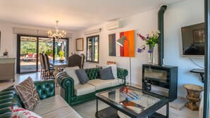 Ein modernes Wohnzimmer mit einem grünen Sofa, einem Glastisch und einem Fernseher. Durch die Glastüren ist ein Essbereich mit Tisch und Stühlen zu sehen.