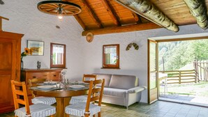 A dining area with a round wooden table, four striped chairs, a grey sofa, and a wooden ceiling. - Rustico Girasole by Interhome (Leontica)