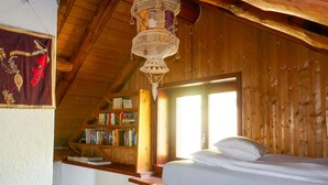 A cozy attic bedroom with a wooden ceiling, a bed, a bookshelf, and a hanging light fixture. - Rustico Girasole by Interhome (Leontica)