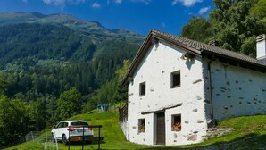 A white building with a sloped roof, a wooden door, and windows with flower boxes. - Rustico Girasole by Interhome (Leontica)