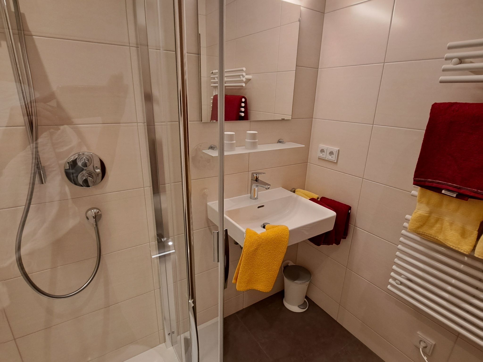 Et moderne badeværelse med en glasafskærmet brusekabine, en hvid vask og et spejl.
