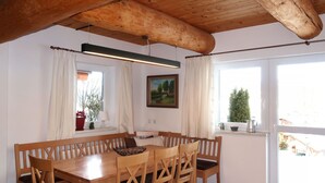 Ein Essbereich mit Holztisch und -stühlen, einem Gemälde an der Wand und fenster mit Vorhängen.