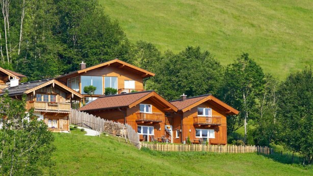 Eine Holchhütte mit mehreren Balkonen, gelegen an einem Hang mit Holzzaun und üppiger Vegetation.