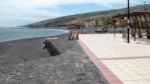 A beach with a paved walkway, a wooden bench, and a rocky area.