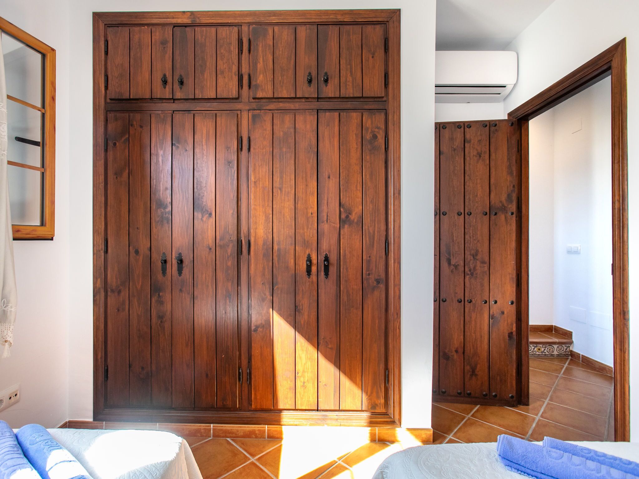 A bedroom with a large wooden wardrobe, a bed with a white duvet, and a bathroom with a shower.