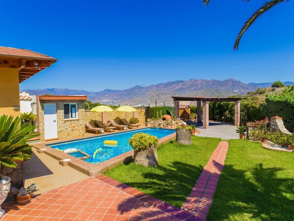 Uma área de piscina com vista para montanhas, uma pérgula e um pequeno edifício.