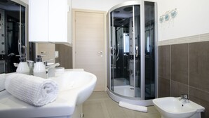 Un baño moderno con ducha de vidrio, lavamanos blanco y un espejo grande.