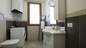 Baño pequeño con lavadora, inodoro, lavamanos y perchero para toallas.