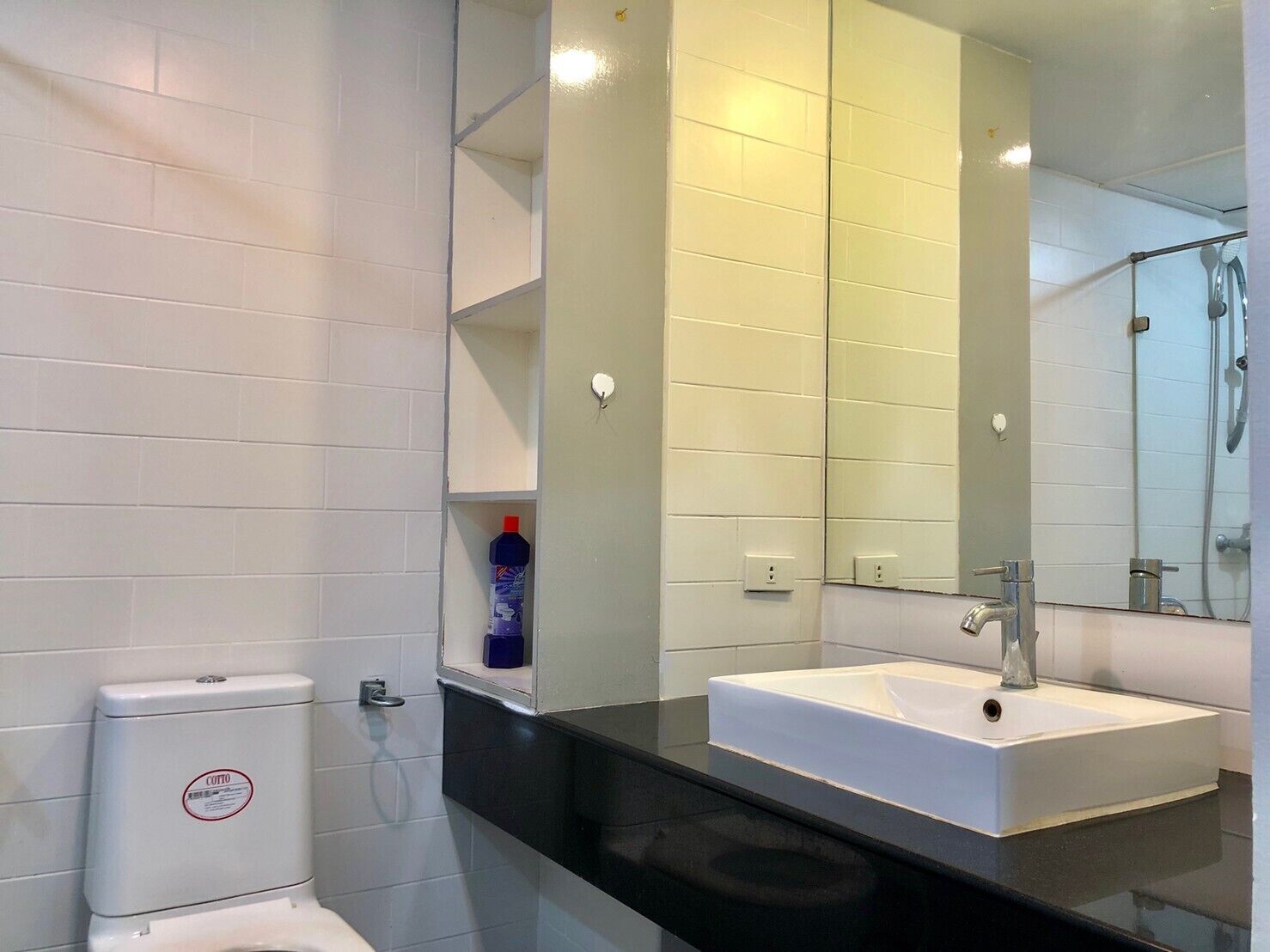 A modern bathroom with a white toilet, a black countertop, a white sink, and a large mirror.