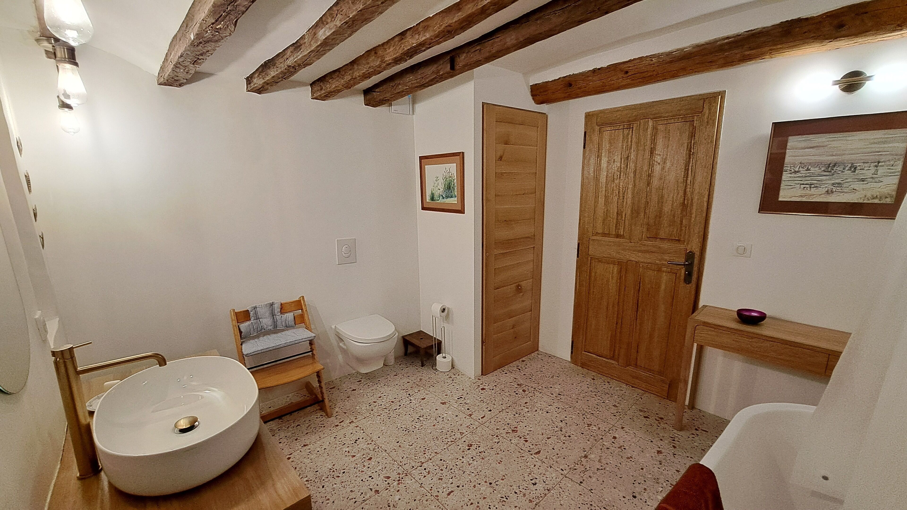Un baño con una bañera independiente, una silla de madera, un inodoro y una puerta de madera.