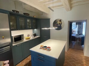 Eine Küche mit dunkelblauen Schränken, einer weißen Arbeitsplatte und einem Essbereich, der durch einen offenen Durchgang zu sehen ist.