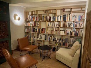 Ein gemütliches Wohnzimmer mit Bücherregal, zwei Ledersesseln, einem runden Couchtisch und einem cremefarbenen Sofa.