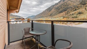 A balcony with wicker chairs and a glass table overlooking a mountainous landscape.