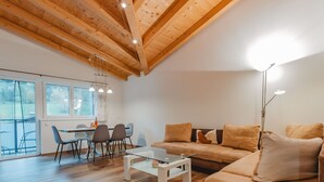 A spacious living room with a wooden ceiling, a sofa, a coffee table, and a dining area with chairs and a table.