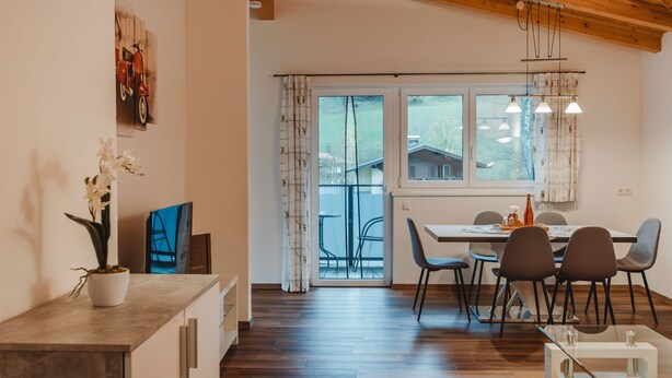 A modern kitchen with wooden flooring, a dining area with a table and chairs, and a large window with curtains.