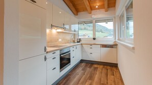 A modern kitchen with white cabinets, a wooden ceiling, and a view of a green landscape through a window.
