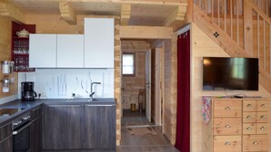 A modern kitchen with dark cabinets, a coffee maker, and a wooden staircase leading to a living area with a TV and storage drawers. - Vacation home Waltl by Interhome (Fusch)