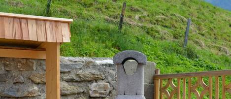 An outdoor stone pizza oven with a wooden roof, a stack of firewood, and a stone wall.