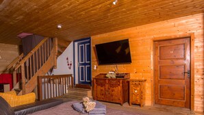 Un interior acogedor de cabaña de madera con una cama grande, un televisor montado en la pared, una escalera y una puerta de madera.