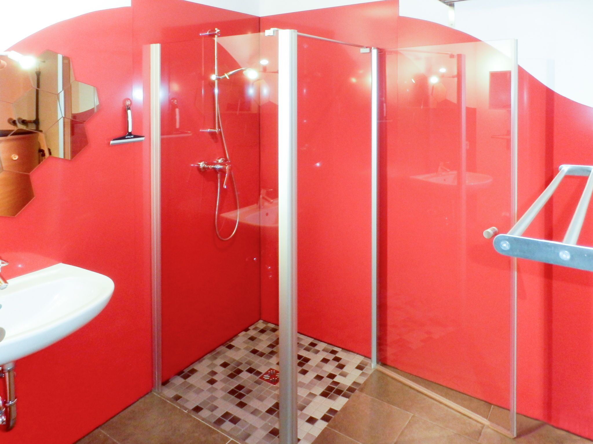 Un baño moderno con cabina de ducha de vidrio, un lavabo blanco y un suelo de baldosas rojas.