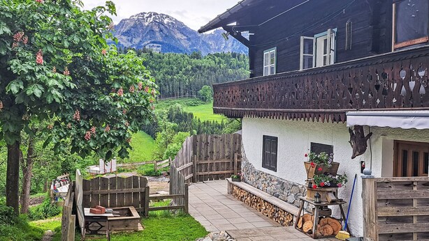 Una cabaña tradicional con cimientos de piedra, balcón de madera y vistas a un paisaje montañoso.