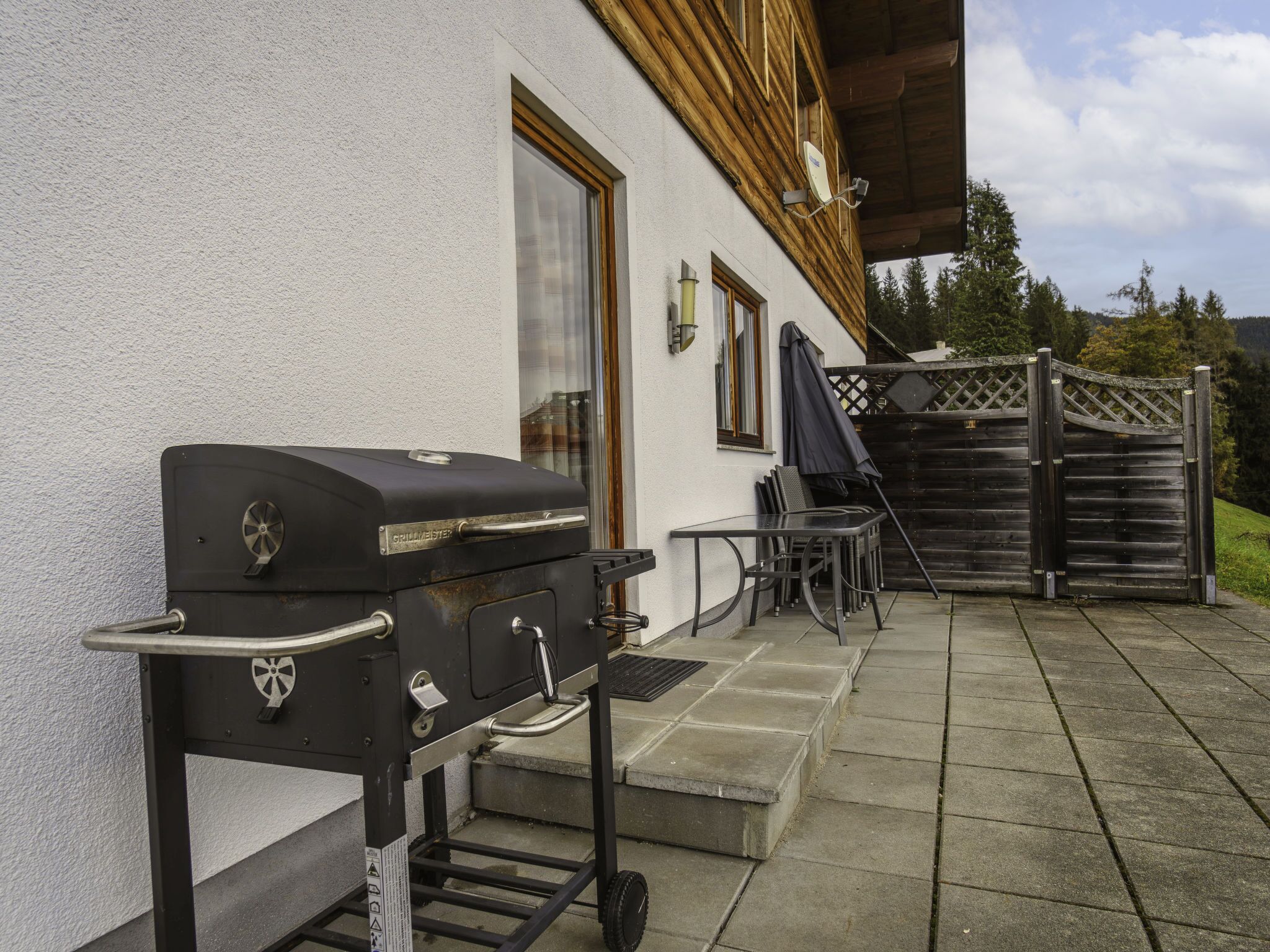 A grill outside a building with a patio area, a table, and a gate.