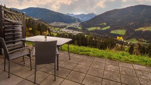 Un espace extérieur aménagé avec une table et des chaises, offrant une vue sur une vallée, des montagnes et une ville au loin.