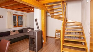 Une pièce chaleureuse avec un plafond en bois, un canapé, un petit radiateur et un escalier en bois.