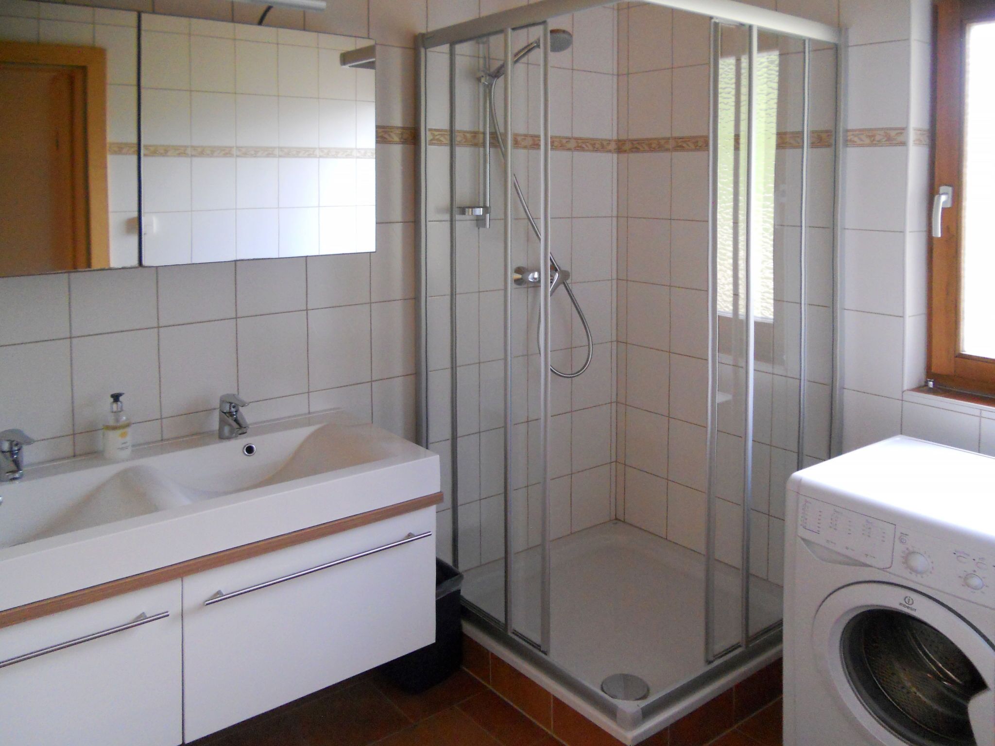 Ett badrum med en dusch som är avskärmad med glasväggar, ett vitt handfat och en tvättmaskin.