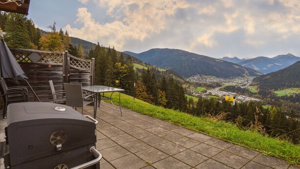 An outdoor patio with a grill, chairs, and a table overlooking a valley with mountains and a town. - Vacation home Auer by Interhome (Eben im Pongau)
