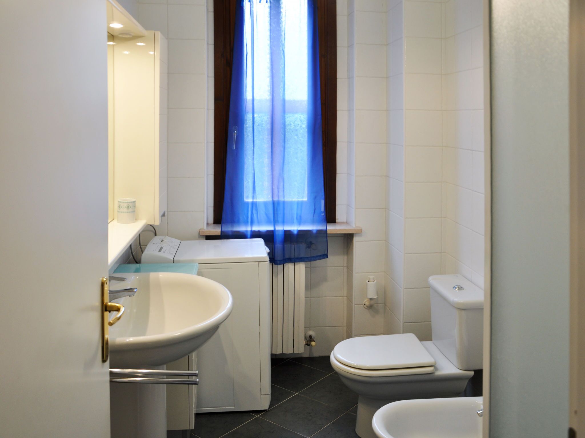Un baño pequeño con lavamanos, inodoro y ventana con cortina azul.
