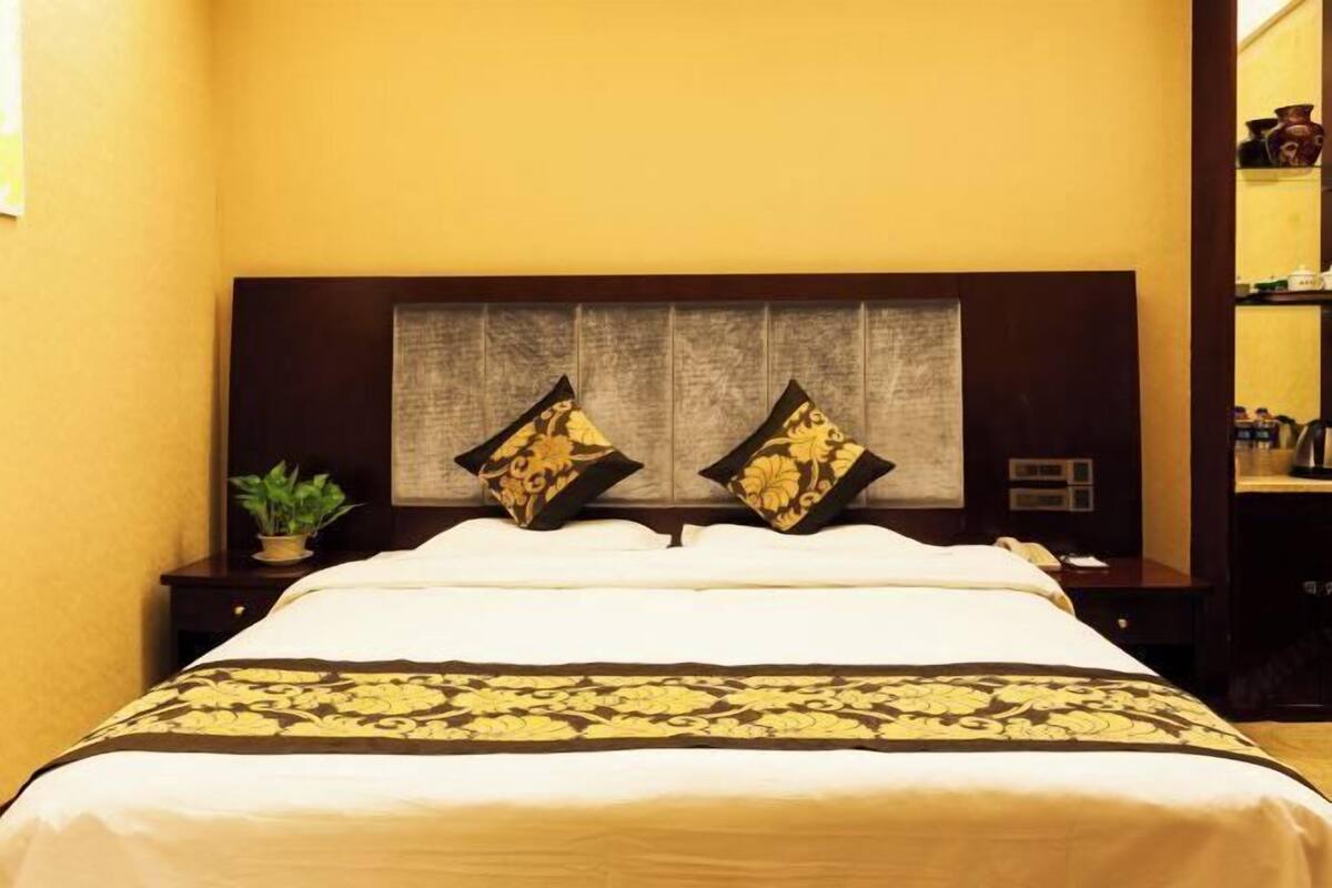 A hotel room with a large bed, two decorative pillows, a nightstand, and a small plant.