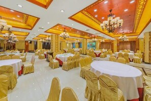 A banquet hall with round tables, chairs, and chandeliers.