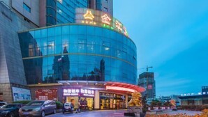 A modern hotel with a curved glass facade, a prominent entrance with a red awning, and a visible parking area. - Jinjiang Hotel (Hanzhong)