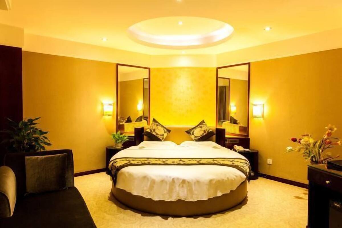 A hotel room with a round bed, two bedside tables, a large mirror, and a ceiling light fixture.