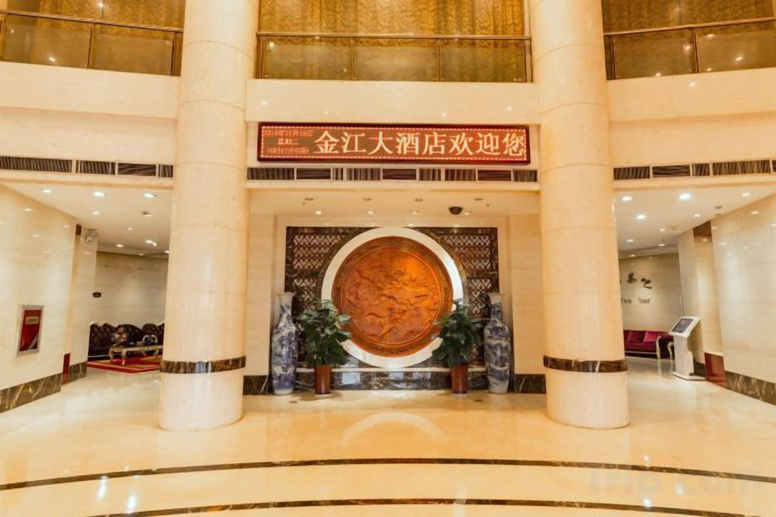 Un vestíbulo de hotel con un gran muro decorativo circular, una recepción y un área de descanso con sofás.