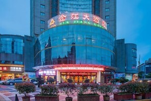 A hotel with a curved glass facade, illuminated signage, and a central entrance with a canopy. - Jinjiang Hotel (Hanzhong)