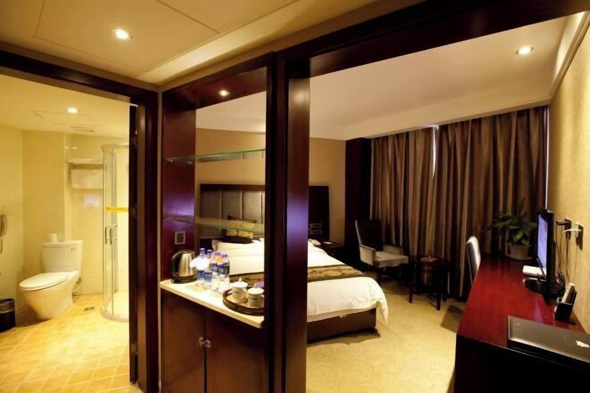 A hotel room with a bed, desk, chair, and a shower area.