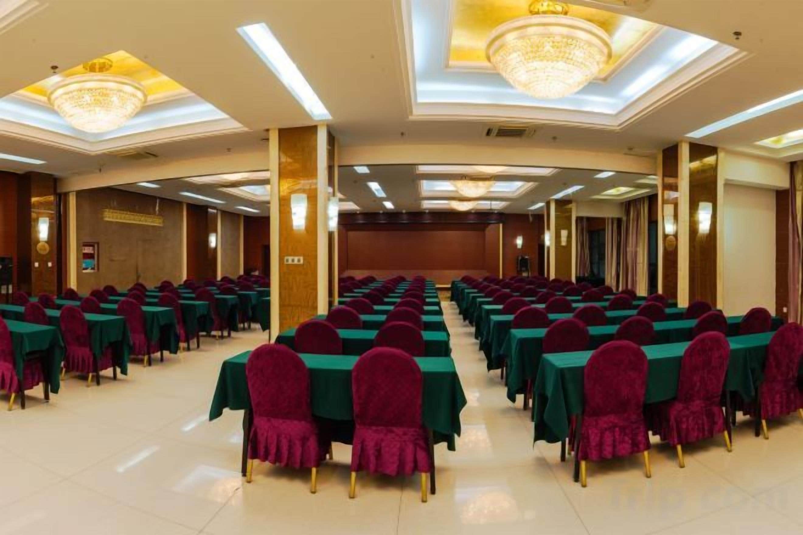 A banquet hall with rows of tables and chairs, a stage, and chandeliers.